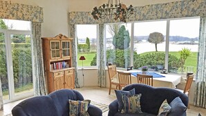 A cozy living room with a view of a lake, a wooden cabinet with books, and two armchairs with floral cushions. - "Seeschwalbe" Vacation Rental in Kappeln (Kappeln)