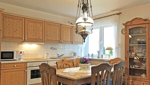A kitchen with wooden cabinets, a dining table with chairs, a hanging light fixture, and a cabinet with glass doors. - "Seeschwalbe" Vacation Rental in Kappeln (Kappeln)