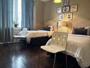 Two single beds with matching headboards and sheer curtains frame the room's large window.