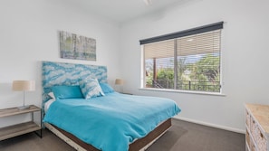 A bedroom with a bed, two bedside tables, a window with blinds, and a wall-mounted artwork. - H2O Holiday Apartments - Unit 5 (NORTH HAVEN)