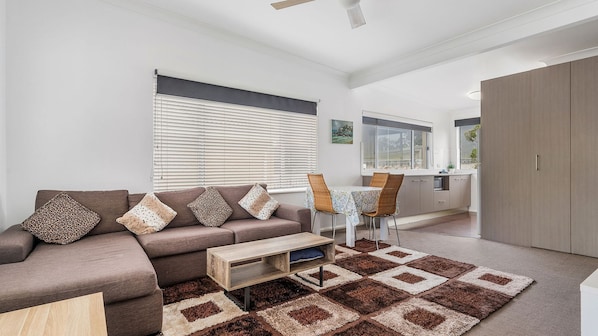 A modern living room with a sofa, coffee table, and a dining area with chairs and a table. - H2O Holiday Apartments - Unit 5 (NORTH HAVEN)