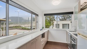 A compact kitchen with a large window, a built-in oven, and a sink. - H2O Holiday Apartments - Unit 5 (NORTH HAVEN)
