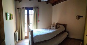 A bedroom with a single bed, a radiator, a window with curtains, and a door.