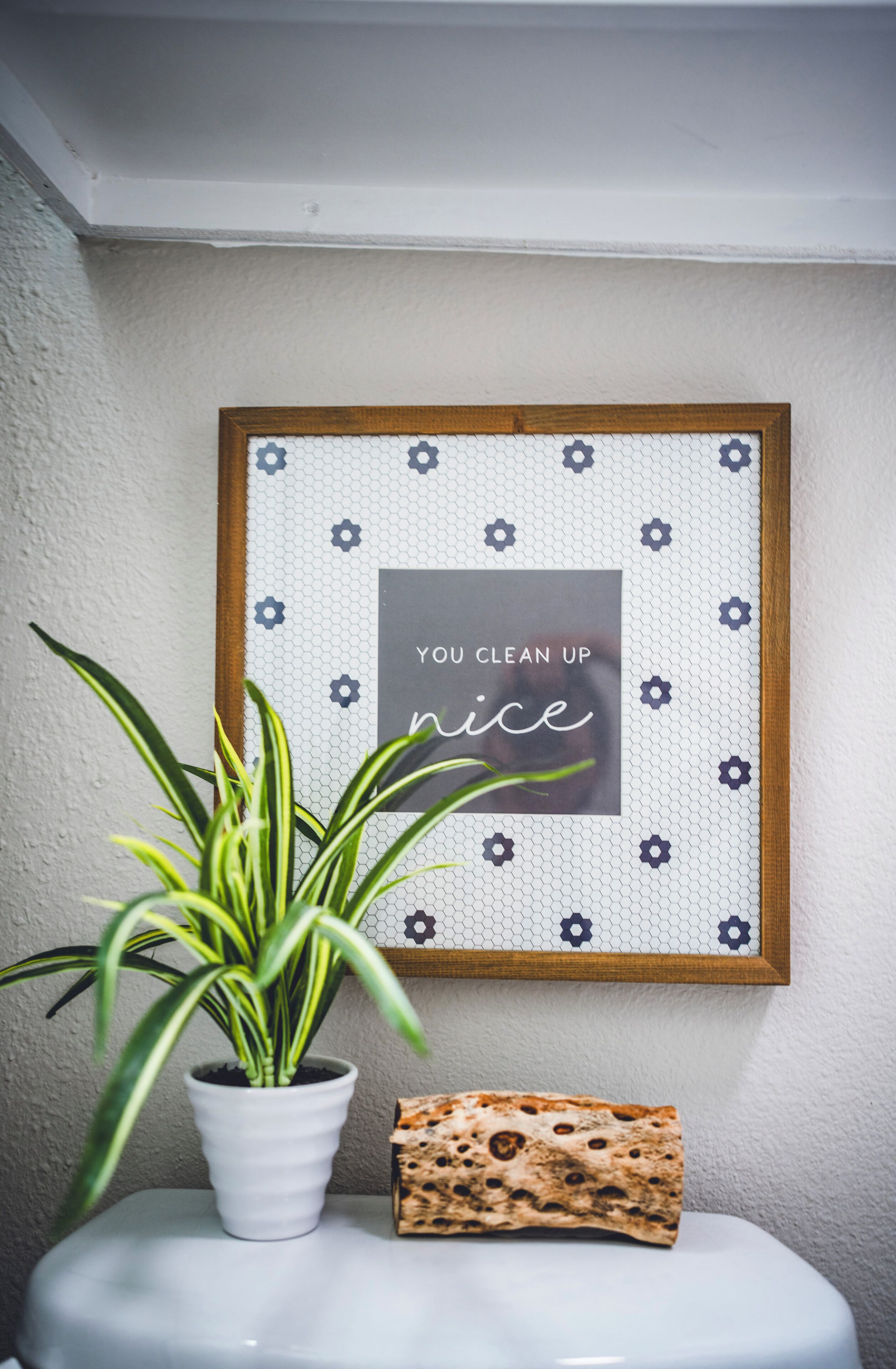 A framed quote on a wall, a potted plant, and a rolled-up mat on a white surface.