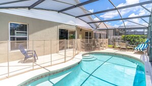A covered outdoor swimming pool with a glass ceiling, surrounded by a fence, and equipped with lounge chairs and a table. - 3 Minutes to Disney — Windsor Palms Single Level home w Private Pool, Game Room, & Expansive Patio (Kissimmee)