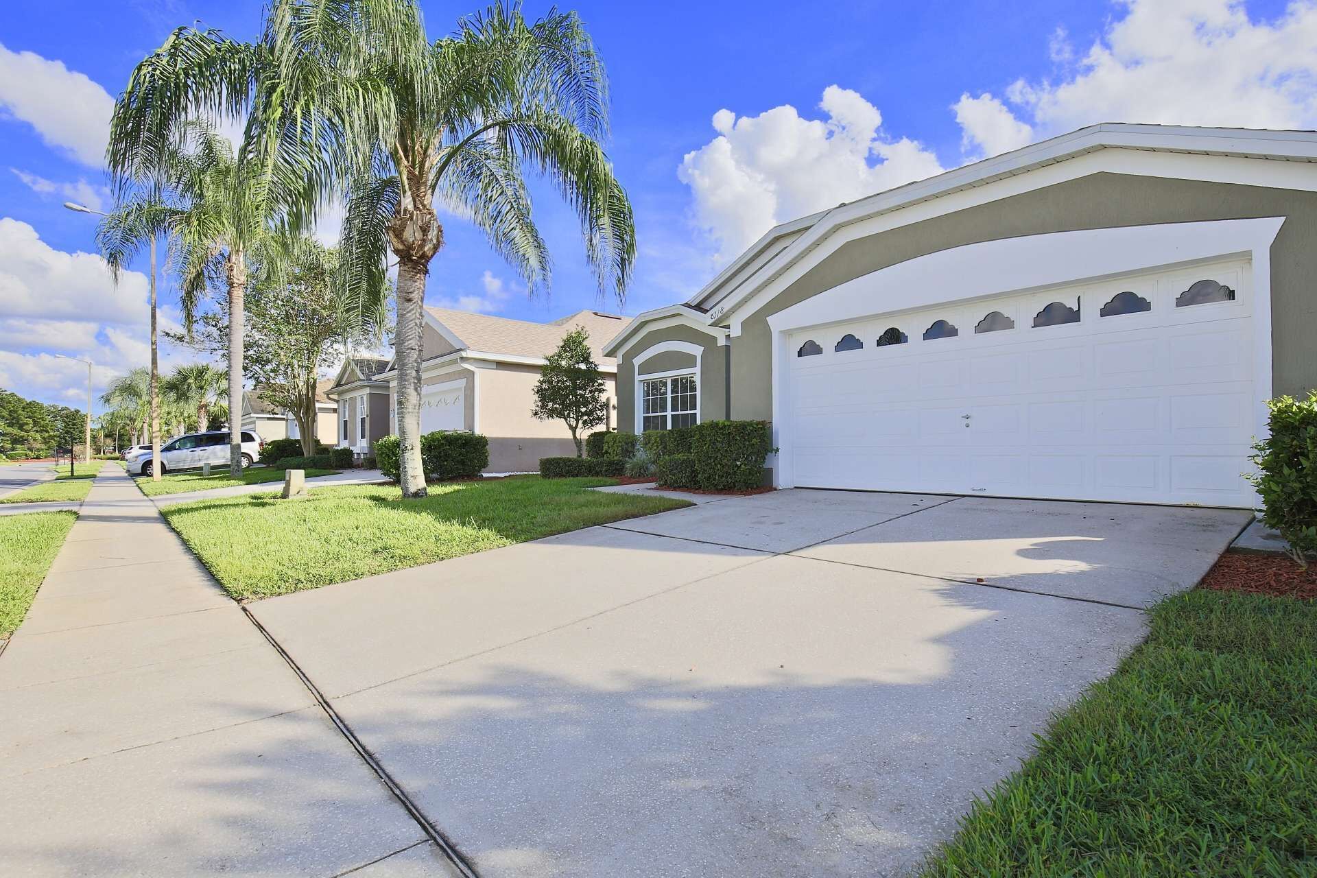 A residential street with houses, palm trees, and a clear sky.