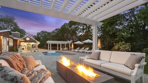 An outdoor patio with a pool, a fire feature, and a white sofa.