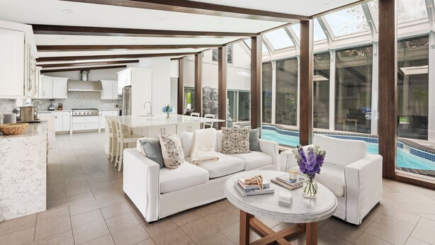 A spacious living area with a white sofa, a dining table, and a view of a swimming pool.