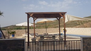 Une terrasse au bord de la plage, agrémentée d’une pergola en bois, de chaises longues et d’une piscine.
