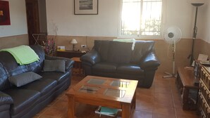 Un salon avec deux canapés en cuir, une table basse en bois, un lampadaire et une fenêtre avec des stores.