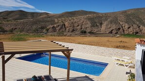 Un espace piscine agrémenté d’une pergola, de chaises longues et offrant une vue sur les collines.