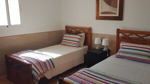 Une chambre avec deux lits simples, chacun agrémenté d’un oreiller à rayures et d’une table de chevet avec deux lampes.
