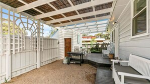 A covered patio with a grill, seating area, and a view of the neighborhood.