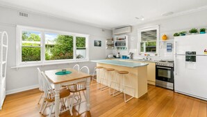 A modern kitchen with a central island, bar stools, a dining table with chairs, a refrigerator, and a stove.