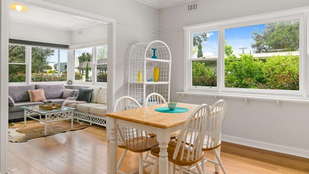 A bright room with a wooden dining table, white chairs, a white sofa, and a white bookshelf.