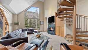 Ein geräumiges Wohnzimmer mit einem großen Ecksofa, einem Kamin und einer Holztreppe.