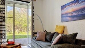 En stue med sofa, puder, et bord med æbler, et maleri og en skydedør til en have.