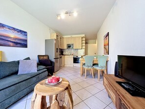 A compact living space with a sofa, a dining table with chairs, a TV, and a kitchen area with cabinets and appliances.