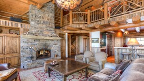A cozy log cabin interior with a stone fireplace, wooden furniture, and a balcony overlooking the interior.