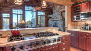 A spacious kitchen with a large stove, wooden cabinets, and a stone fireplace.
