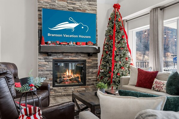 A cozy living room with a fireplace, a Christmas tree, and a sign for Branson Vacation Houses.