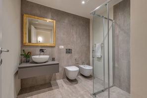 A modern bathroom with a large mirror, a vessel sink, a bidet, and a glass-enclosed shower.