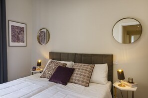 A neatly made bed with pillows, a bedside table with a lamp, a framed picture, and a round mirror on the wall. - Luxury 4-bedroom, 4-bathroom apartment. (Firenze)