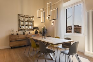 A dining area with a wooden table, multiple chairs, a modern chandelier, and a large mirror on the wall.