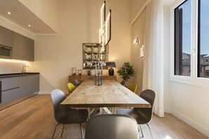 A modern dining area with a wooden table, black chairs, a potted plant, and a kitchen in the background. - Luxury 4-bedroom, 4-bathroom apartment. (Firenze)