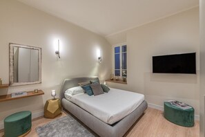 Quarto moderno com cama, abajures, televisão, janela e espelho.