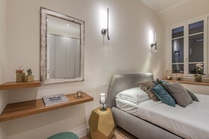 A bedroom with a bed, bedside tables, a mirror, and a window.