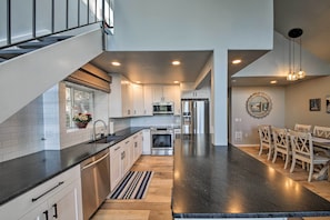 A modern kitchen with white cabinets, a black countertop, stainless steel appliances, and a dining area with wooden chairs.