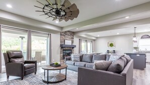 Ein großzügiges Wohnzimmer mit Kamin, Deckenventilator und einer Küchenzeile im Hintergrund.
