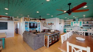 A spacious living area with a large sofa, a wooden dining table, and a kitchen area with white cabinets and blue accents. - OV23 Shared Pool, Pet Friendly, Golf Cart Access (Port Aransas)