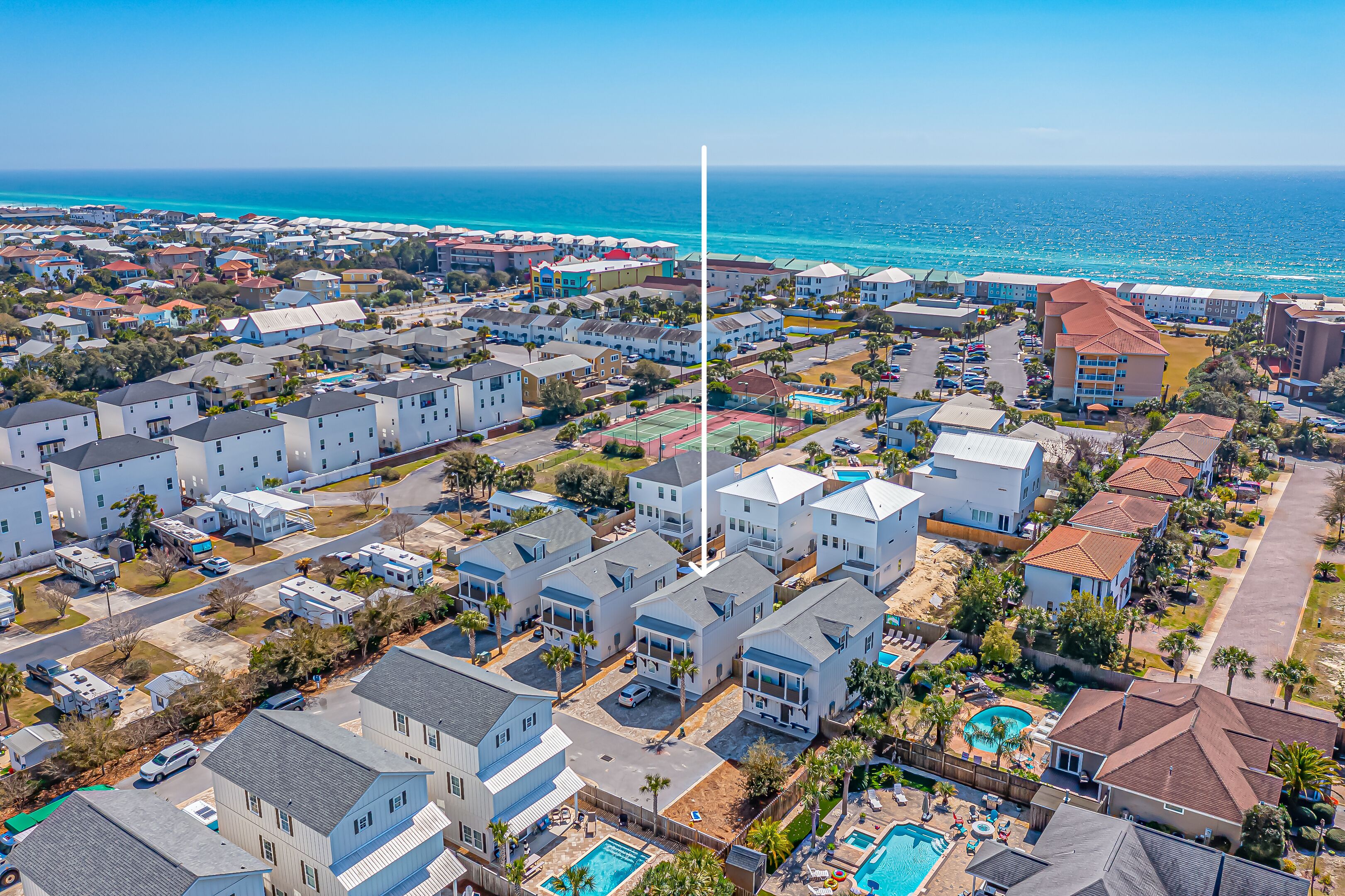 Vue aérienne d’un quartier résidentiel situé sur la côte, avec des maisons, une piscine et une plage en arrière-plan.