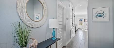 Un couloir avec un miroir rond, une lampe bleue et une sculpture de poisson posée sur une console.