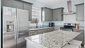 A modern kitchen with granite countertops, stainless steel appliances, and grey cabinetry. - Private Pool ~ Golf Cart ~ Walk to the Beach (Miramar Beach)