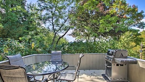 An outdoor patio with a glass-top table and metal chairs, surrounded by a wooden deck and a barbecue grill. - House w/ Balcony ~ 5 Mi to Cranmore Resort! (Bartlett)