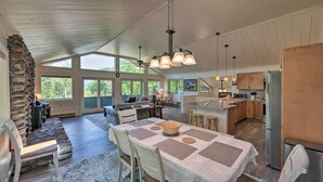 A spacious kitchen with wooden cabinets, a stainless steel refrigerator, and a dining area with a table set for four. - House w/ Balcony ~ 5 Mi to Cranmore Resort! (Bartlett)