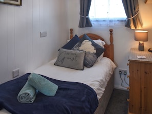 A neatly made bed with a rolled towel, a bedside lamp, and a wall socket. - 2 bedroom accommodation in Brundall, near Norwich (Brundall, near Norwich)