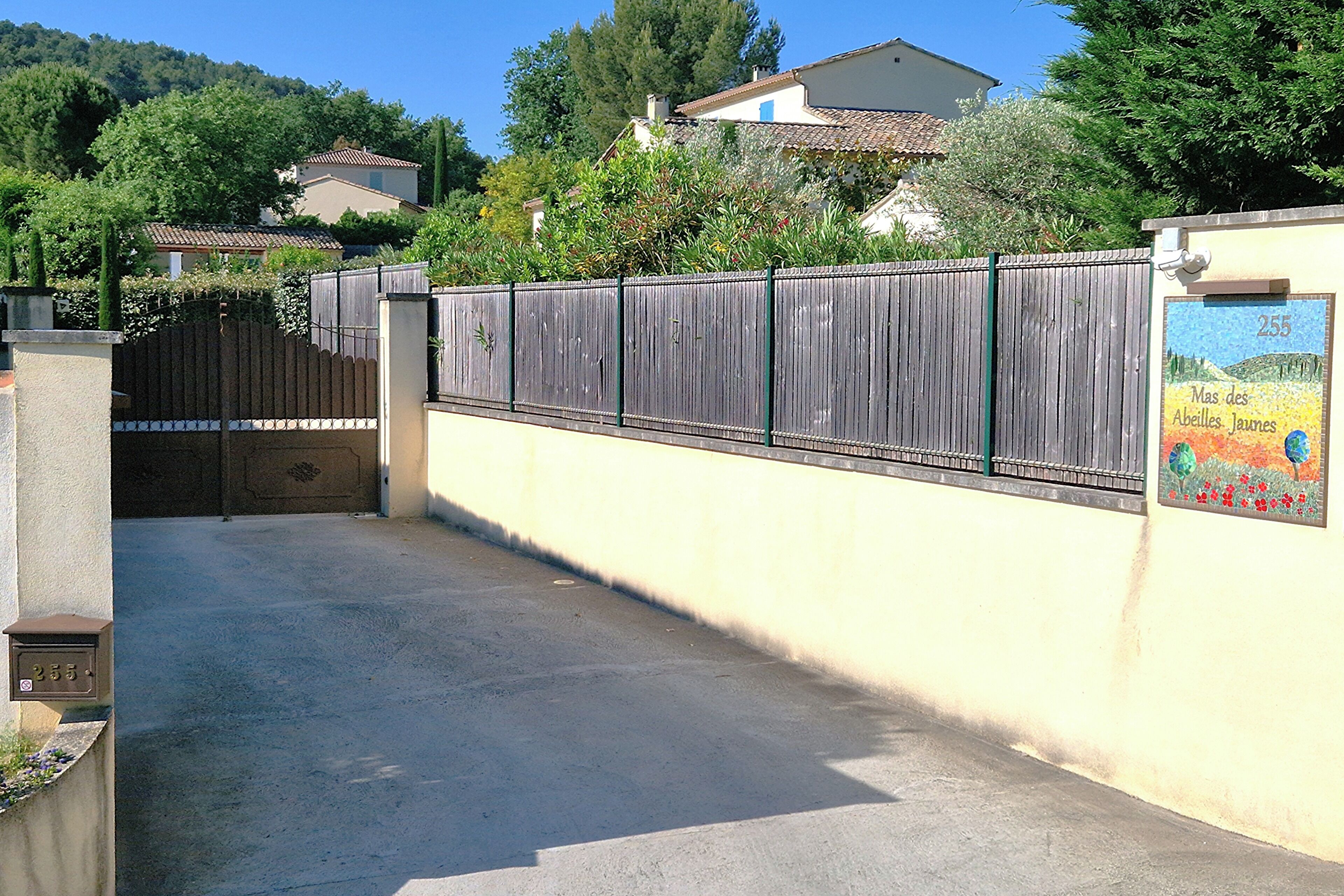 A gated driveway leading to a residential area with a mailbox and a wall with a number sign.