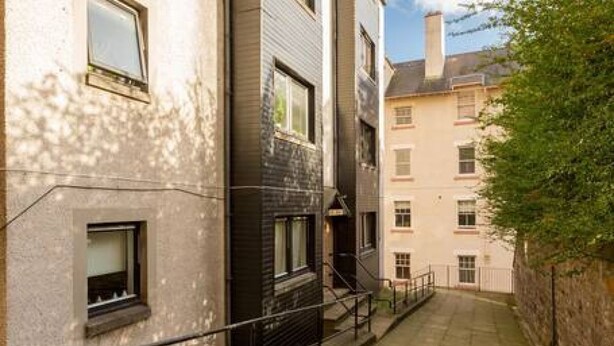 Une ruelle étroite, bordée de bâtiments, avec un mur de pierre d’un côté et une rambarde métallique de l’autre.