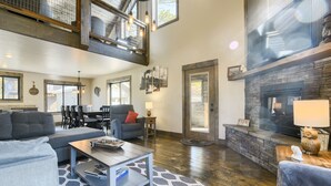 A spacious living room with a high ceiling, a fireplace, and a dining area with a view of the outdoors.