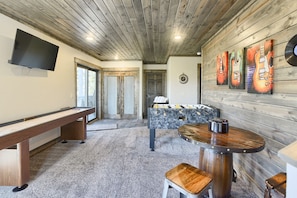 A cozy room with a wooden ceiling, a foosball table, a TV, and a wall with guitar paintings.
