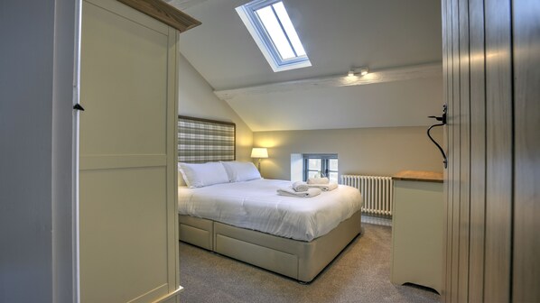 Un dormitorio con cama, ventana, radiador y tragaluz.