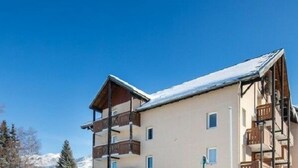 A multi-story building with balconies, likely a hotel or resort, with a snowy mountain backdrop.