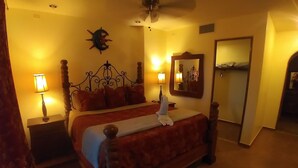 Habitación de hotel con una cama de madera, dos lámparas de noche, una mesita de noche, un espejo y un ventilador de techo.