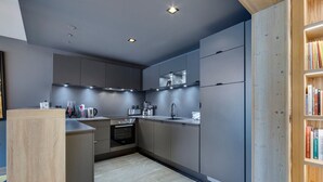 Une cuisine moderne avec des meubles gris, un four encastré et une bibliothèque en bois.