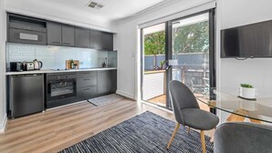 A modern kitchen with a built-in oven, a dishwasher, and a large window overlooking a balcony. - Noble House~2 Bed/1Bath/1Car~Parklands + Transport (Wilston)