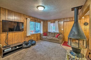 Un salon chaleureux avec des murs en bois, un téléviseur à écran plat, un canapé, une cheminée et un tapis rouge.